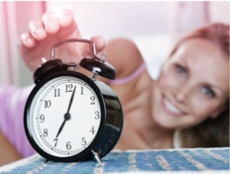 Foto di una sveglia con una donna sullo sfondo che allunga un braccio per spegnere la suoneria.